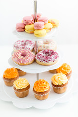 fast food and sweets concept - glazed donuts, cupcakes and macarons on stand over white background