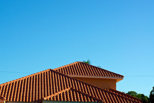 View of three orange terra cotta clay roof tops against a clear blue sky in bonita springs florida with deep shadows from morning light.