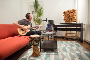 Musician playing electric guitar in home music studio.