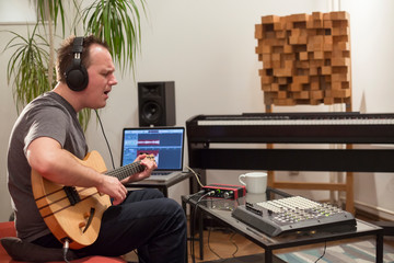 Musician playing electric guitar in home music studio.