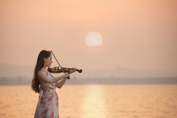 Beautiful woman playing violin at  the sea with sunrise background © ittipol
