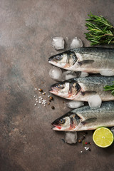 Fresh raw seabass fish with rosemary and lime on a dark brown rustic background. Flat lay, top view, copy space.