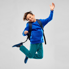 school, education and people concept - happy smiling student boy with bag jumping over grey...