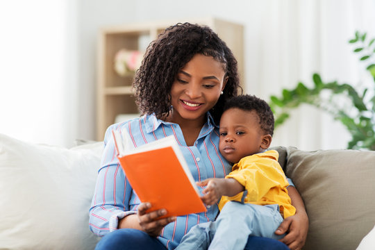 childhood, kids and people concept - happy african american mother with book and her baby son at home