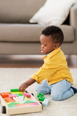 childhood, kids and people concept - lovely african american baby boy playing with wooden toy blocks kit on floor at home