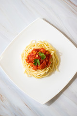 Pasta with fresh tomatoes, cooked with olive oil and garlic on a light background and a white square plate. Italian food. Vertical orientation