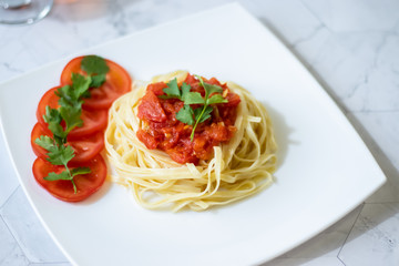 Pasta with fresh tomatoes, cooked with olive oil and garlic on a light background and a white square plate. Italian food. Horizontal orientation