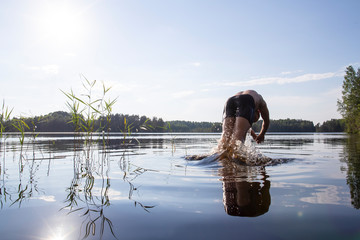 A man bathes and jumps into a clean forest lake, in which his reflection is visible, against the...
