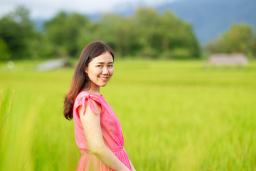 Happy and beautiful Asian woman's portrait in the rice and meadow field close up with natural blurred background.  Asian pretty girl in vintage pink dress portrait in meadow close up.