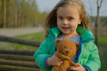 Smiling baby girl holding teddy bear outdoors.