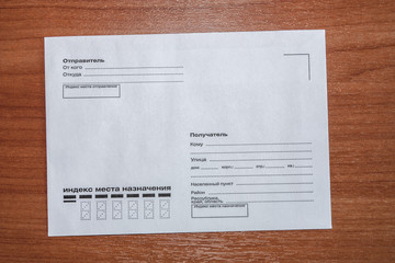 Top view of a postal envelope close-up with unfilled fields for the address of the sender and recipient and the zip code in Russian on an orange wooden table.