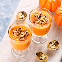 Healthy pumpkin smoothie with walnuts and cinnamon in glasses on rustic background