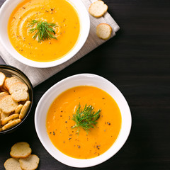 Pumpkin cream soup with croutons and fresh dill and parsley on dark wooden background, top view