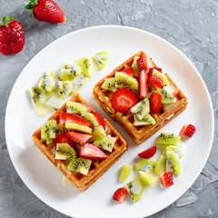 Belgian waffles with fruits strawberries and kiwi on white plate closeup