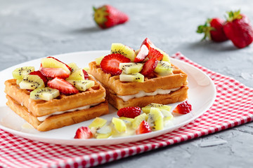 Belgian waffles with fruits strawberries and kiwi on white plate closeup
