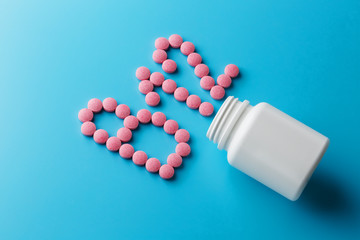 Pink pills in the shape of the letter B12 on a blue background, spilled out of a white can.