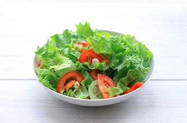 salad of lettuce, tomatoes and cucumbers in a plate on a light wooden background