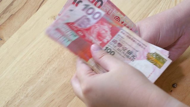 Woman hand counting 100 Hong Kong Dollars banknote, HKD money on wood table