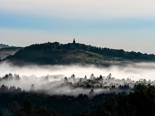 Fototapeta na wymiar Church on the hill and beautiful white fog with sun rays, Alsace