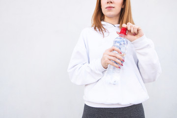 Cropped close-up of a sports girl wearing white clothes, holding a bottle of water in the water on a white background. Fitness girl with a bottle of water in his hand is isolated on white.Copyspace