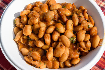 Close of a large portion of white beans cooked with tomato sauce and hot spices in display at a street food market