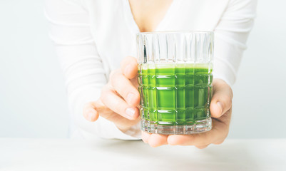Close view of the glass with Japanese Matcha tea in womans hands on light background with copy space.