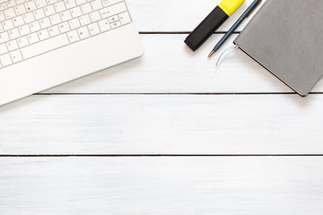 Laptop, highliter, grey notepad and pen on white wooden desk. Top view. Free place for text