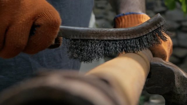 Close-up of a man's hands in work gloves, cleaning the old pipe from rust with a metal brush.