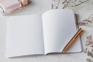 Pink empty paper notebook with golden pen on white table surrounded by flowers and fragrance. The concept of femininity workplace