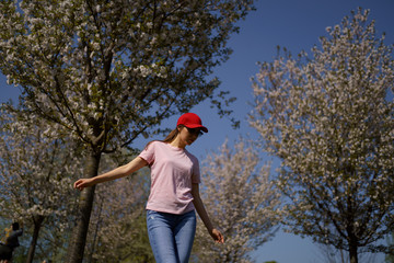 Successful business woman enjoys her leisure free time in a park with blossoming sakura cherry trees wearing jeans, pink t-shirt and a fashion red cap