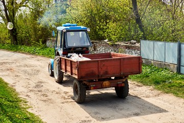 a tractor with a trailer runs through a village street