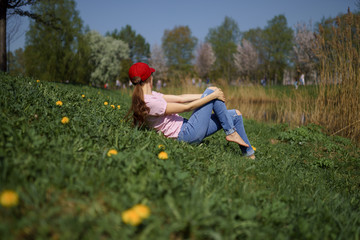 Successful business woman enjoys her leisure free time in a park with blossoming sakura cherry trees wearing jeans, pink t-shirt and a fashion red cap