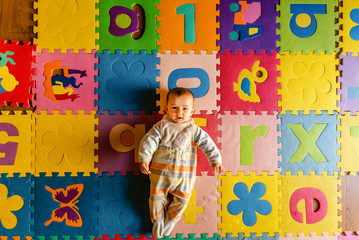 Adorable smiling baby seen from above in pajamas, lying on his back in his toy room.