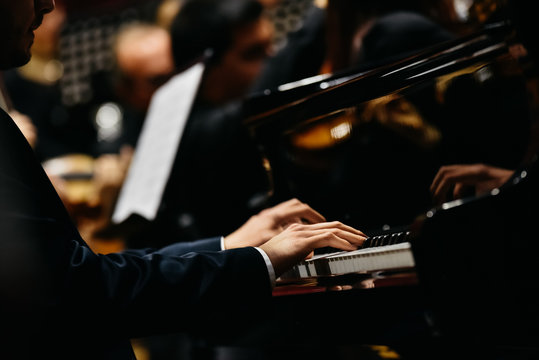 Pianist playing a piece on a grand piano at a concert, seen from the side.