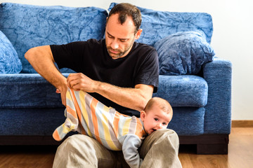 Novice father changing clothes to his baby with effort in the living room of his house.