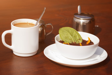 Coffee with milk and creative spring season dessert in bowl (mouse with chocolate powder stylized for spring ground and first green sprouts) 