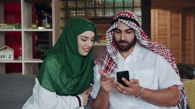 Close Up Emirati Young Couple Use Phone Talk Smile Sitting On Sofa At Home Conversation Atrium Female Lifestyle Culture Arab Indoors Beard Region Smartphone Downtown Emirates Tourism Slow Motion