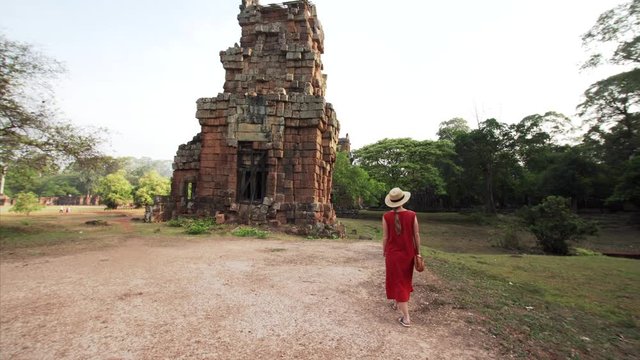 Woman in long red dress is walking near brick ruined Prasat Suor Prat, a series of twelve towers in Angkor Wat complex, made from rugged laterite and sandstone. Cambodia
