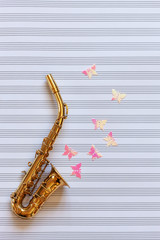 Little Golden saxophone and glitter butterfly figurines. Top view, close-up on note paper background