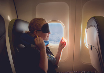 33 year old woman using traveling pillow and sleeping mask in plane cabin on passenger seat, fly...