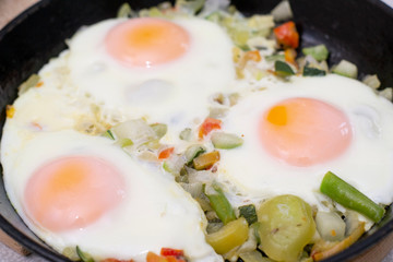 Three eggs with vegatables on frying pan.