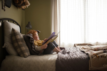 Young boy sitting on bed and looking at book