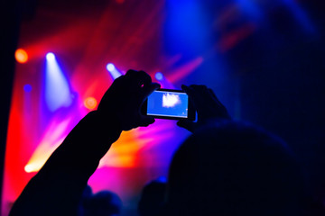Fototapeta na wymiar Man taking photo video by mobile phone of silhouettes crowd party concert music