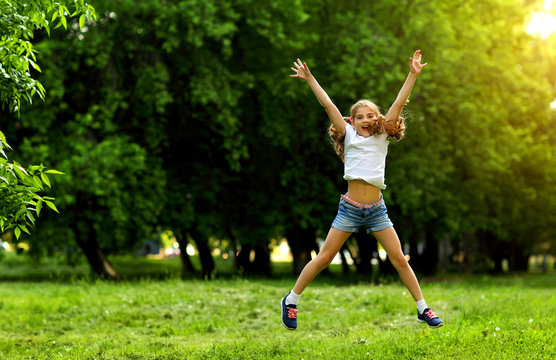 Charming teen girl in shorts and t-shirt jumping and laughing in summer on green background