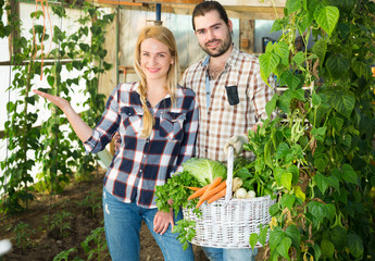 Happy couple with harvested vegetables in greenhouse