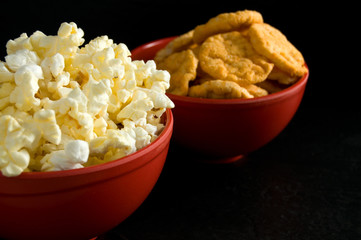 Close Side View of Buttered Popcorn and BBQ Rice Chips in Red Bowls Isolated on Black
