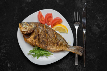 Grilled dorado fish on white dish on black table. Top view.