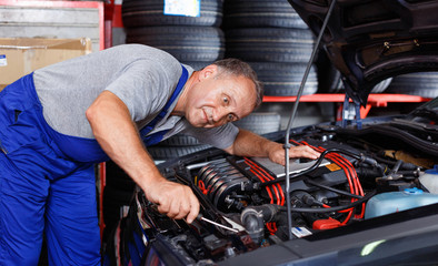 Fototapeta na wymiar Professional mature man car mechanician repairing car in auto repair shop