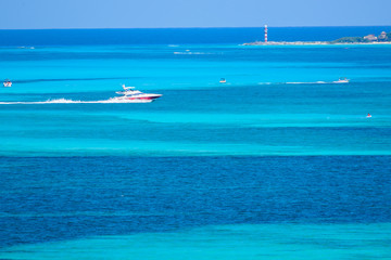 Bote deportivo navegando por el mar caribe con personas disfrutando de un día soleado en el mar caribe de Cancun, Mexico, contraste de colores azul turquesa y faro de navegación al fondo