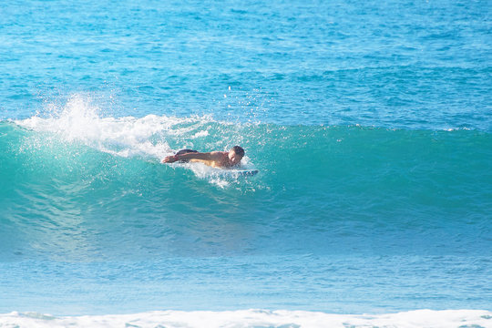 surfer catches a wave in the ocean lying on a surfboard.